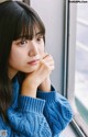 A woman in a blue sweater leaning against a window.