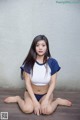 A woman sitting on a wooden floor wearing a blue and white top.