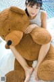 A woman sitting on a bed holding a large teddy bear.