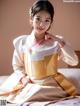 A woman in a white and gold hanbok sitting on a bed.