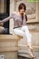 A woman sitting on the steps of a building wearing white pants and a gray top.