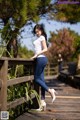 A woman in a white shirt and blue jeans leaning against a wooden fence.