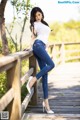 A woman in a white shirt and blue jeans leaning on a wooden bridge.