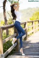 A woman in a white shirt and blue jeans leaning against a wooden fence.