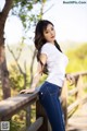 A woman in a white shirt and blue jeans leaning on a wooden fence.