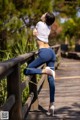 A woman in a white shirt and blue jeans leaning against a wooden fence.