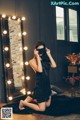 A woman in a black dress sitting on the floor in front of a mirror.