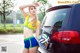 A woman holding a soccer ball next to a car.