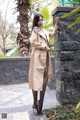 A woman in a trench coat leaning against a stone wall.