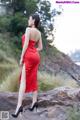 A woman in a red dress standing on a rock.