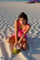 A woman sitting on the beach holding a coconut.