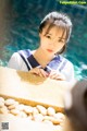 A woman in a sailor outfit leaning on a rock by the water.