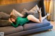 A woman in a green dress laying on a couch.