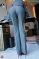 A woman in a gray suit is standing in front of a desk.