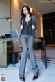 A woman in a suit standing in front of a desk with a laptop.